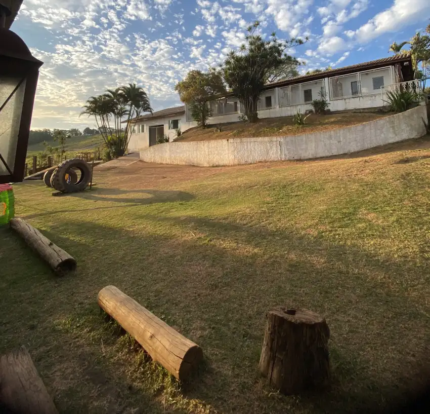 Área de soltura da Dogs 4ever com pneus, troncos e toras de madeira sobre o gramado, bloco de canis ao fundo